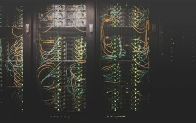 Row of server racks with bundled orange and blue network cables in a data center, illuminated by green activity LEDs.