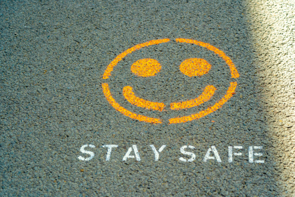 Orange spray-painted smiley on asphalt, with 'STAY SAFE' partially visible beneath.